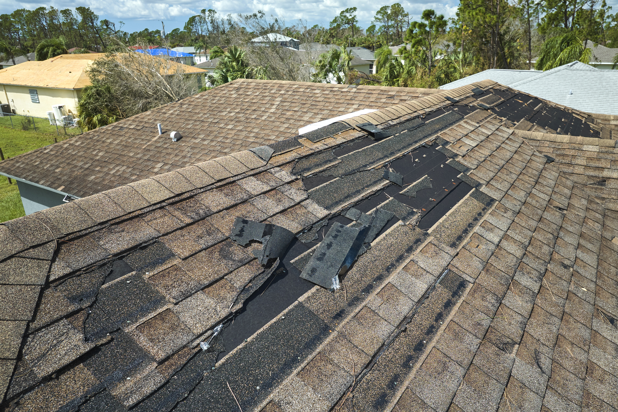 Wind damaged house roof with missing asphalt shingles